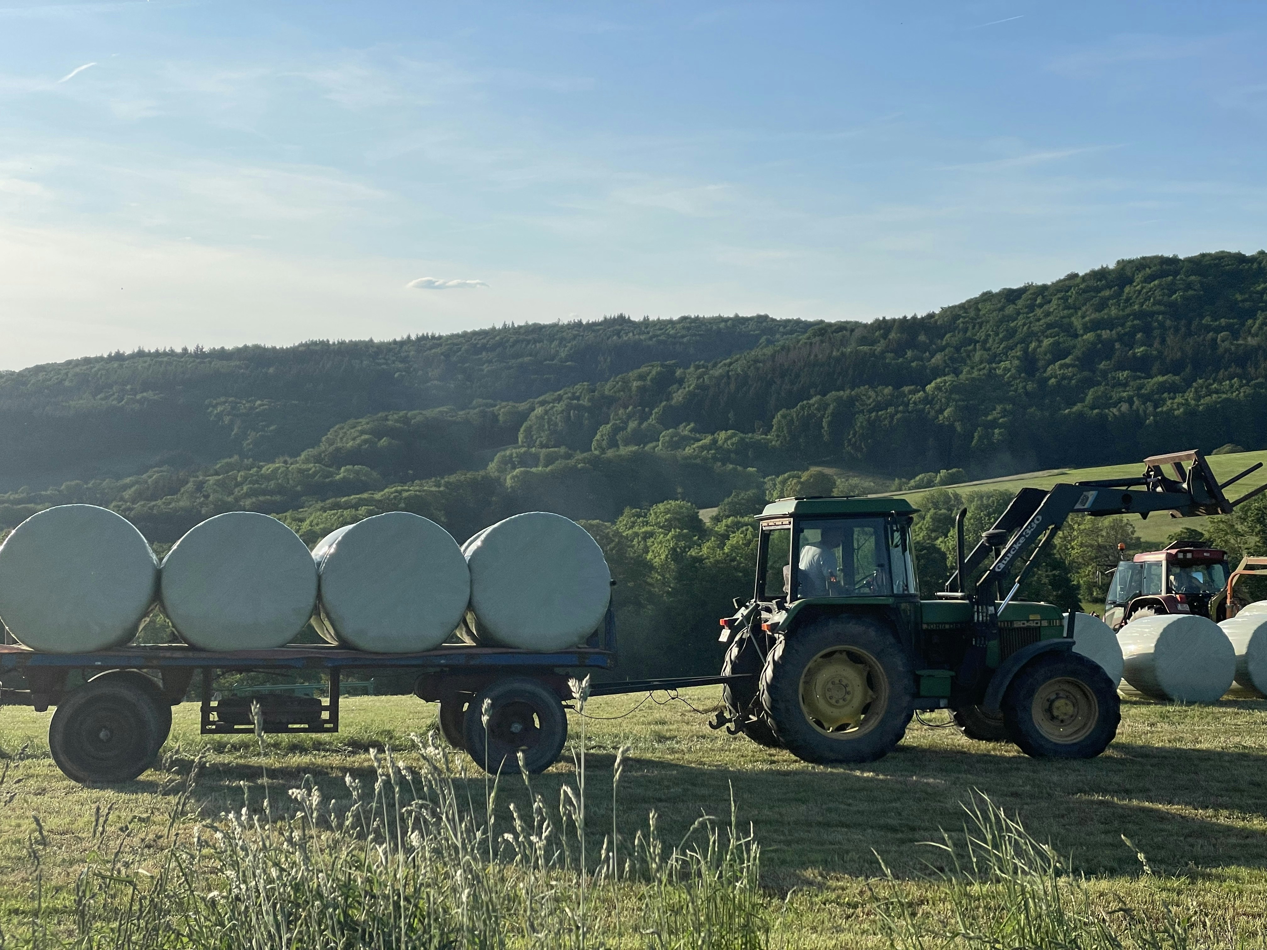 a tractor pulling a trailer full of bales of hay