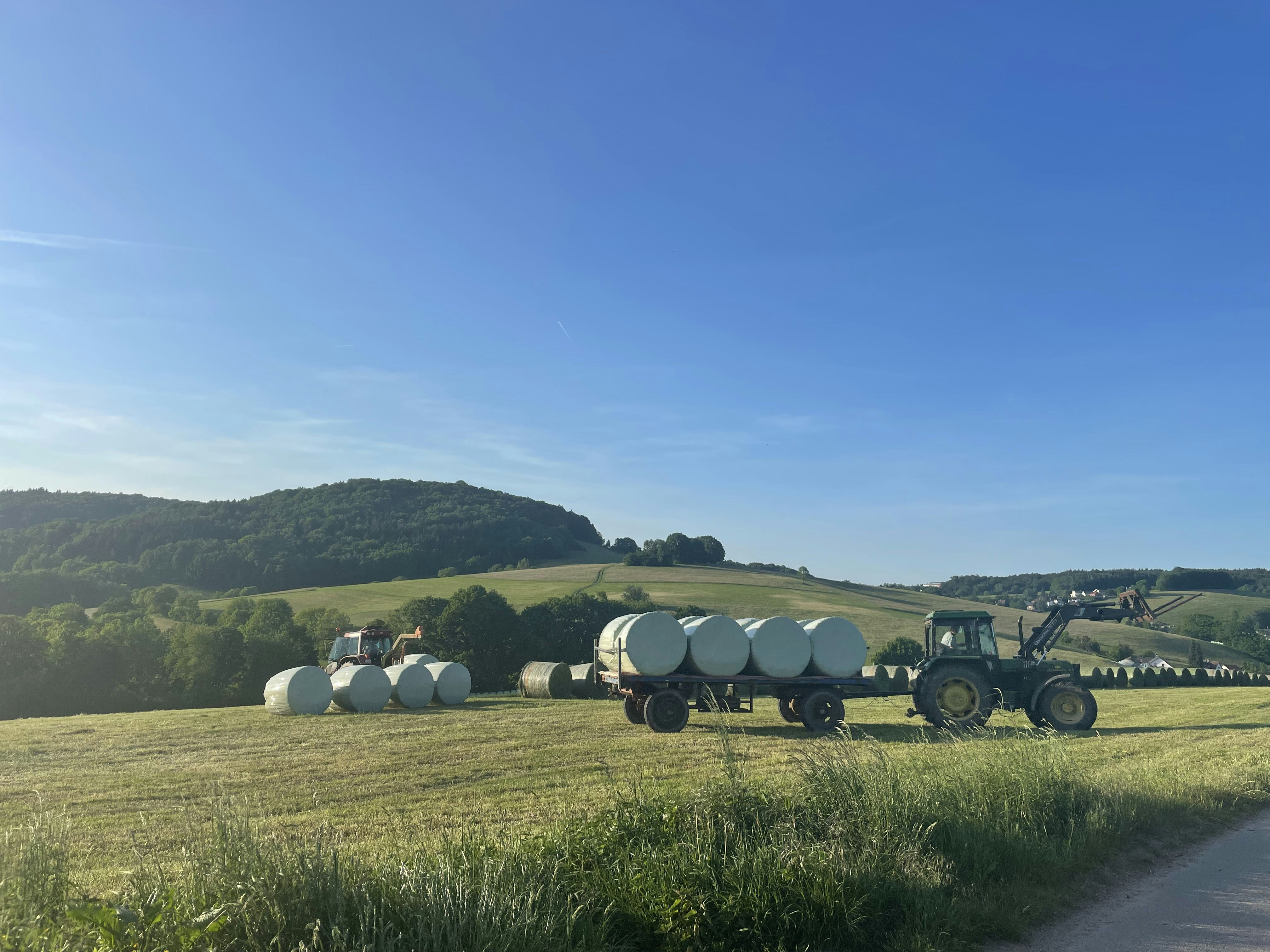 a tractor pulling a trailer full of hay down a country road