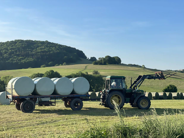 a tractor pulling a trailer full of round bales of hay