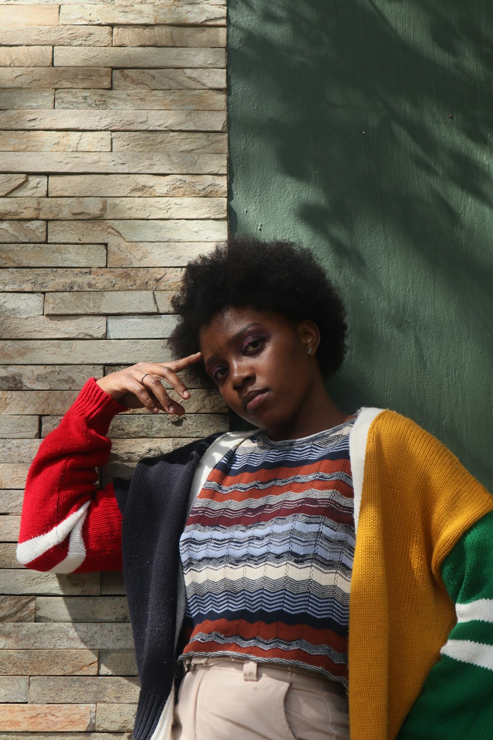 a woman leaning against a brick wall wearing a colorful sweater