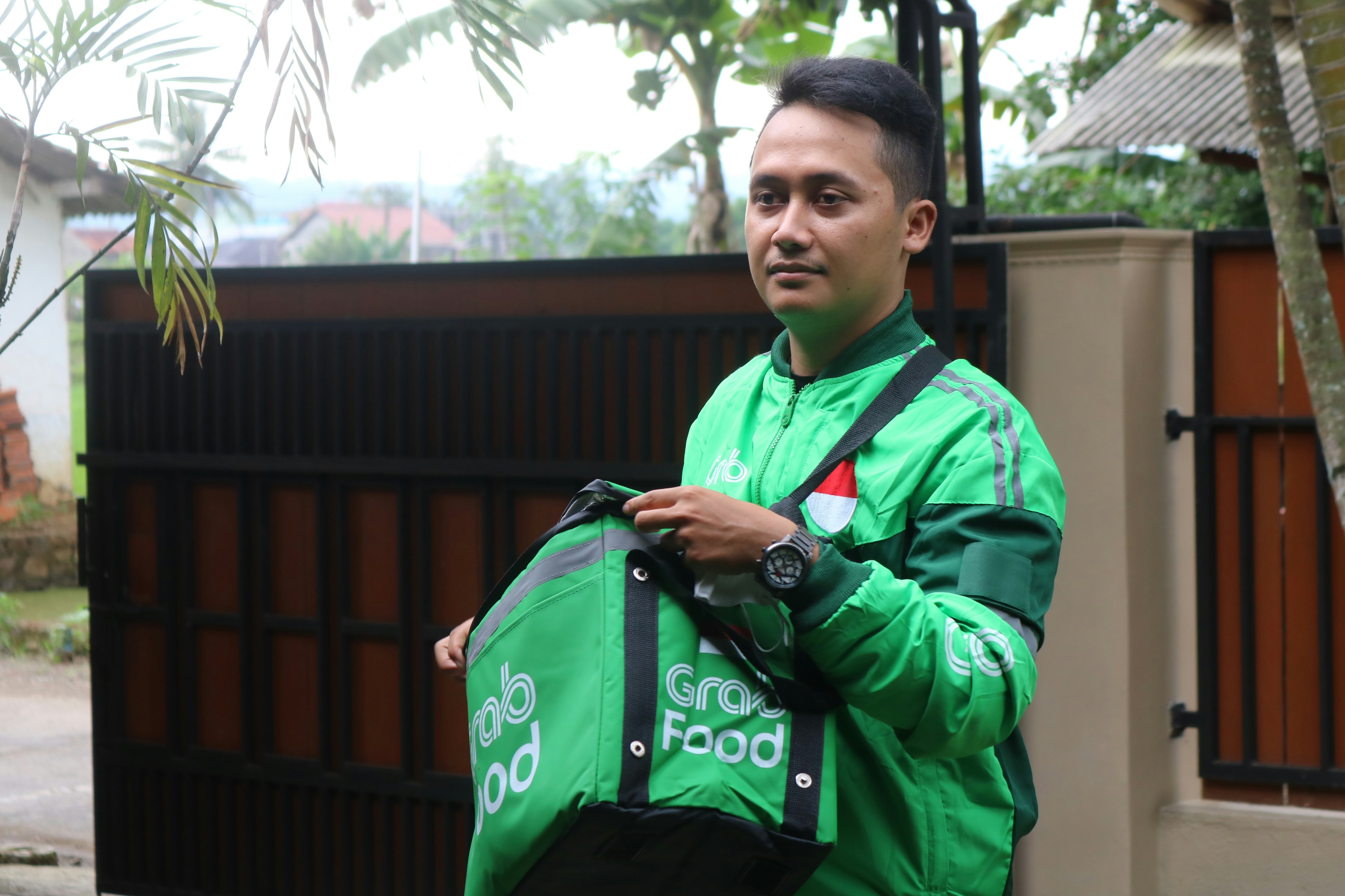 Seorang pria berjaket hijau memegang tas hijau