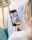 A person is holding a smartphone displaying a social media app with various images. The focus is on the screen, showing an array of lifestyle photos and home decor. The background is slightly blurred, indicating an indoor setting with a chair and table.