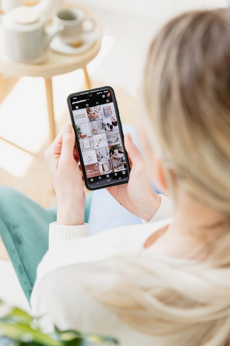 A hand holds a smartphone displaying a shoppable Instagram-style photo grid, similar to a UGC gallery on a product page.