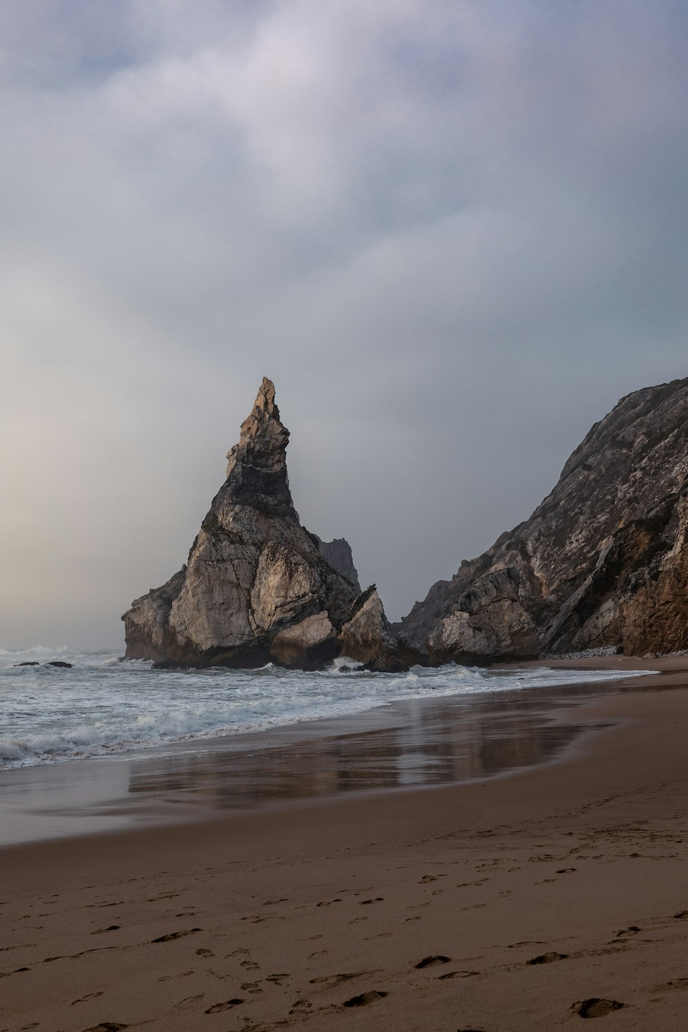 a large rock sticking out of the ocean next to a beach