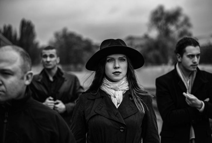 a woman wearing a hat standing in front of a group of men
