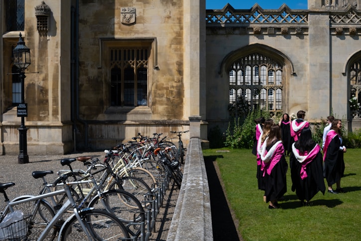 Graduates in pink and black robes walking near bicycles and stone building,symbolizing MBAcompletion