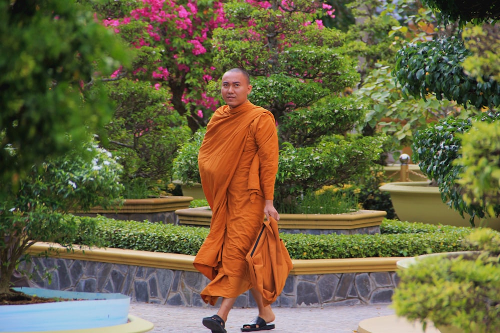 a man in an orange robe walking through a garden