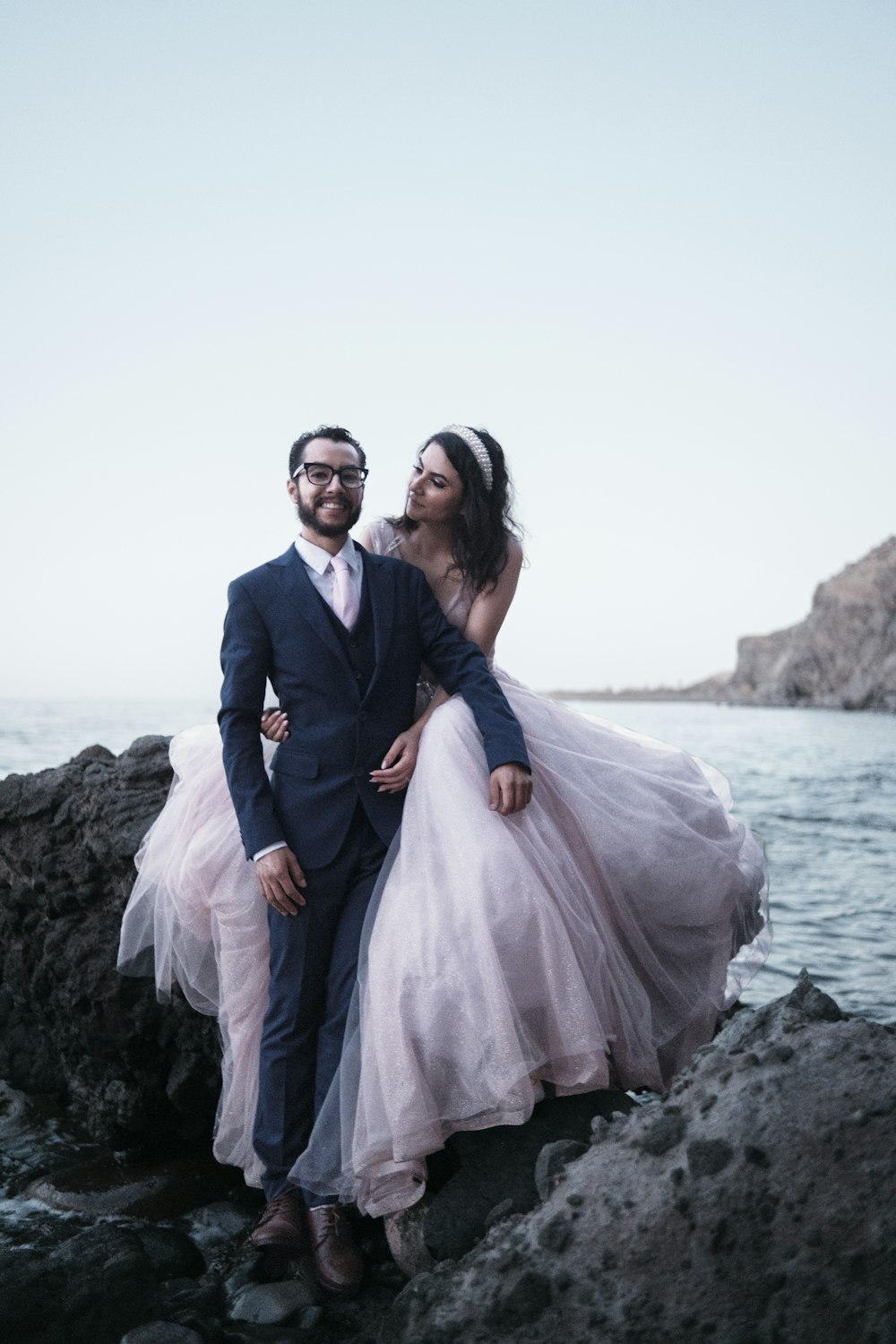 a man and a woman are standing on rocks by the water