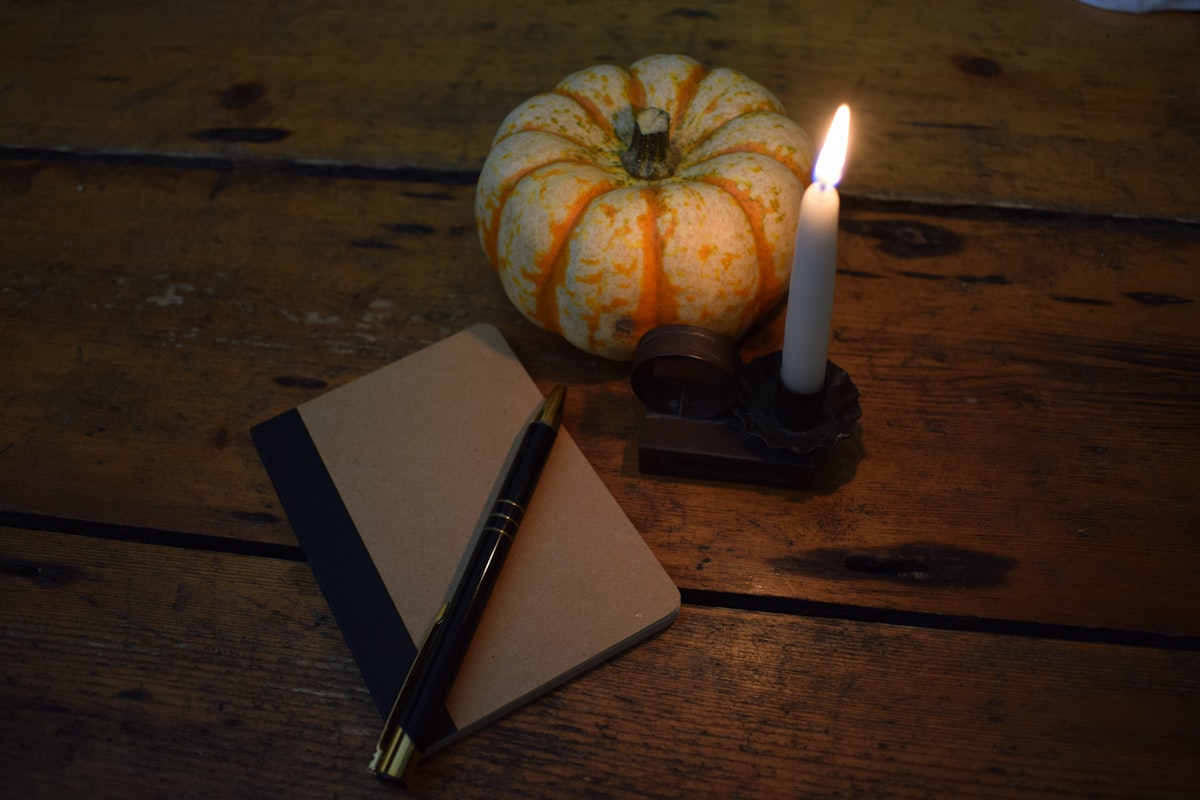 A candle and notebook on a wooden table in warm low light