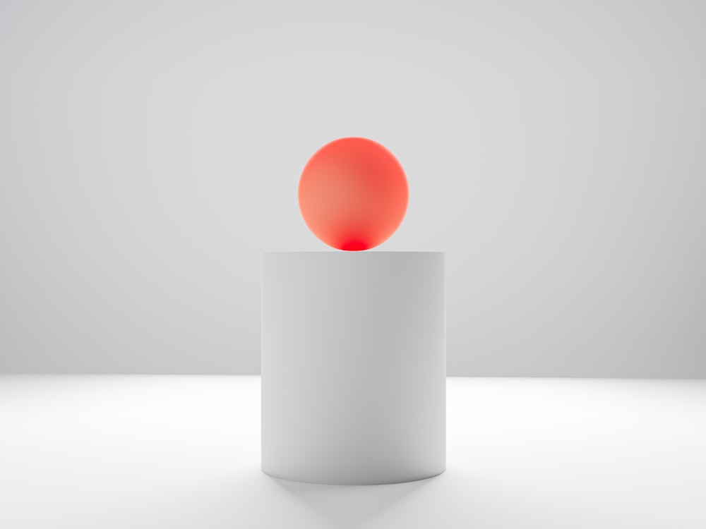 a red ball sitting on top of a white cylinder