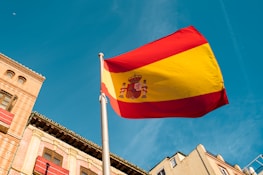 Close-up of hands signing mortgage documents with a Spanish flag in the background.