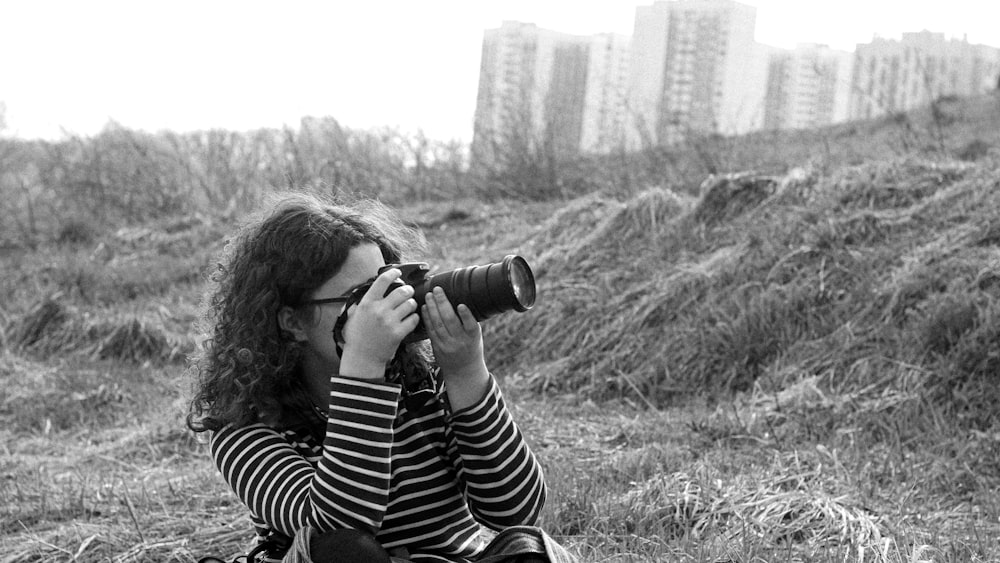 a woman sitting on the ground taking a picture with a camera