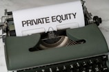 A vintage green typewriter with a sheet of paper inserted displays the text 'PRIVATE EQUITY' in bold letters. The typewriter rests on a white marble surface, and its keys and mechanisms are visible.