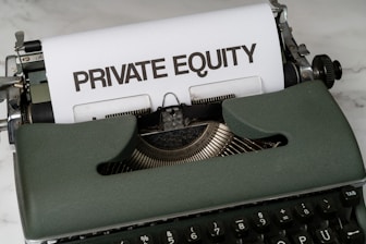 A vintage green typewriter with a sheet of paper inserted displays the text 'PRIVATE EQUITY' in bold letters. The typewriter rests on a white marble surface, and its keys and mechanisms are visible.