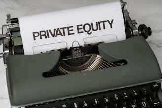 A vintage green typewriter with a sheet of paper inserted displays the text 'PRIVATE EQUITY' in bold letters. The typewriter rests on a white marble surface, and its keys and mechanisms are visible.