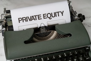 A vintage green typewriter with a sheet of paper inserted displays the text 'PRIVATE EQUITY' in bold letters. The typewriter rests on a white marble surface, and its keys and mechanisms are visible.