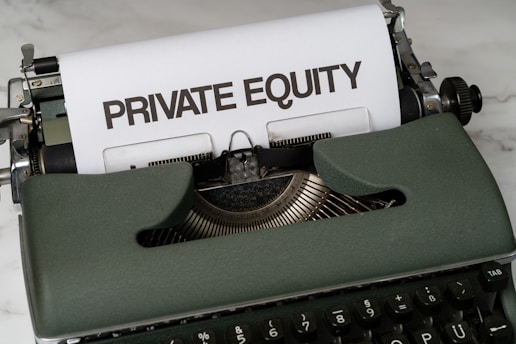 A vintage green typewriter with a sheet of paper inserted displays the text 'PRIVATE EQUITY' in bold letters. The typewriter rests on a white marble surface, and its keys and mechanisms are visible.