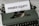 A vintage green typewriter with a sheet of paper inserted displays the text 'PRIVATE EQUITY' in bold letters. The typewriter rests on a white marble surface, and its keys and mechanisms are visible.