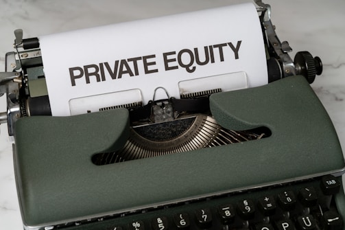 A vintage green typewriter with a sheet of paper inserted displays the text 'PRIVATE EQUITY' in bold letters. The typewriter rests on a white marble surface, and its keys and mechanisms are visible.