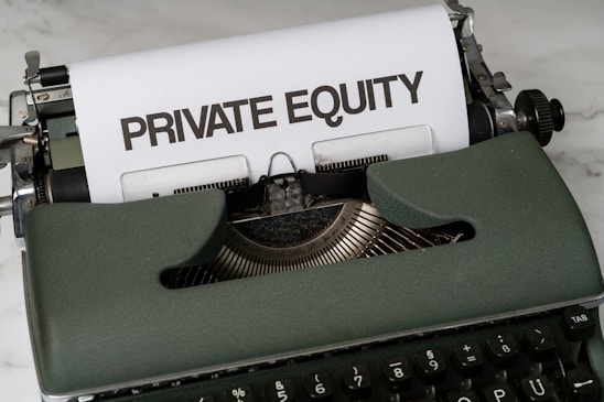 A vintage green typewriter with a sheet of paper inserted displays the text 'PRIVATE EQUITY' in bold letters. The typewriter rests on a white marble surface, and its keys and mechanisms are visible.