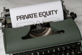 A vintage green typewriter with a sheet of paper inserted displays the text 'PRIVATE EQUITY' in bold letters. The typewriter rests on a white marble surface, and its keys and mechanisms are visible.
