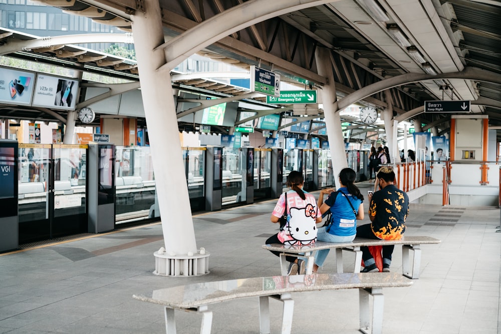 three people sitting on a bench at a train station