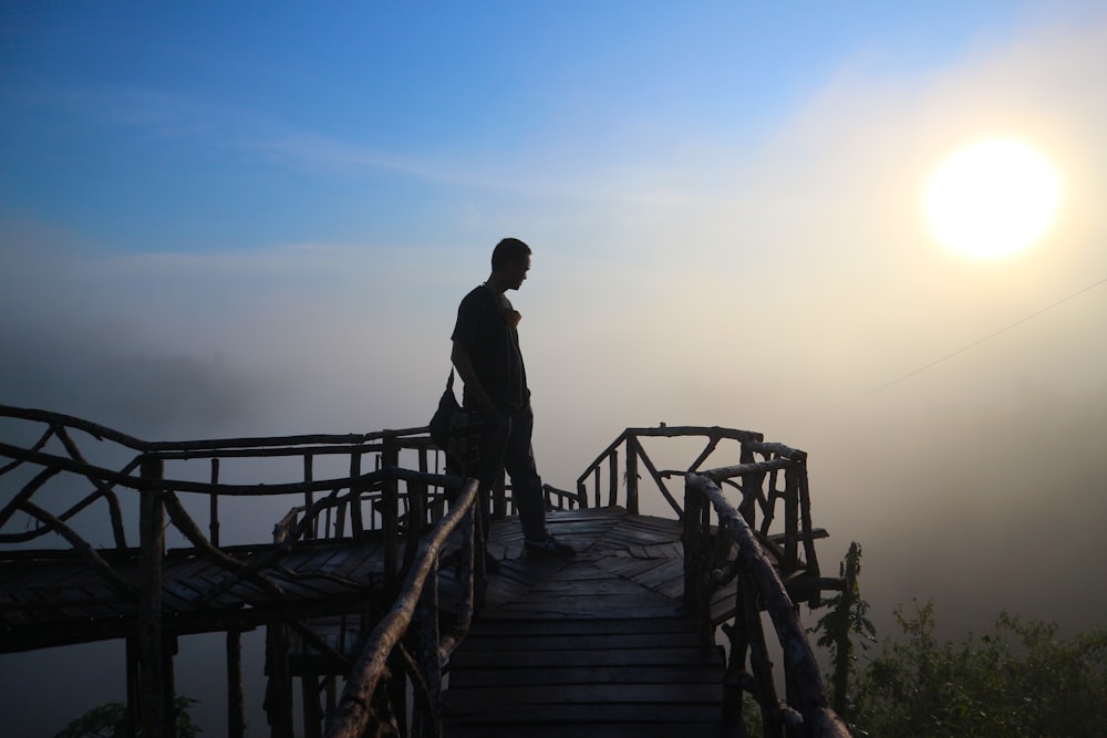 a man standing on a wooden bridge with the sun in the background