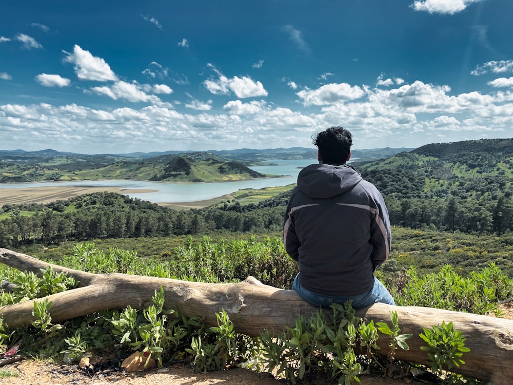 a man sitting on a log looking out over a valley