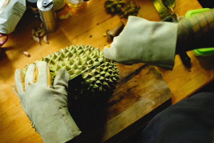 a person cutting a durian fruit on a cutting board