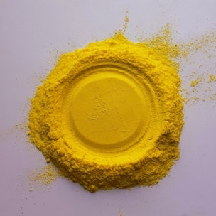 Bright yellow sulfur granules forming a small heap on a clean white background.