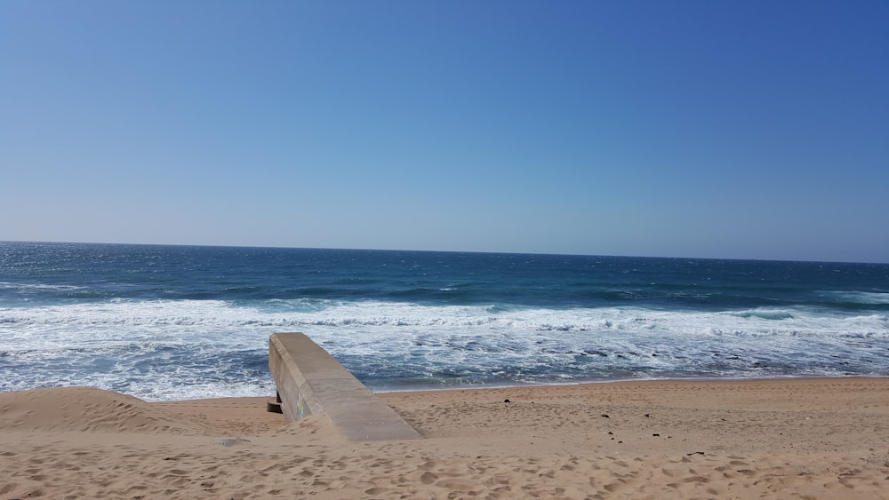 a bench sitting on top of a sandy beach next to the ocean