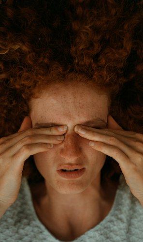 A person resting on a couch in a dim room with their eyes closed