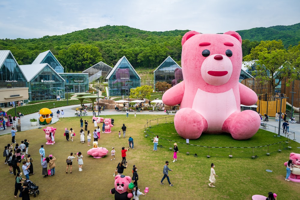 a large pink teddy bear sitting on top of a lush green field