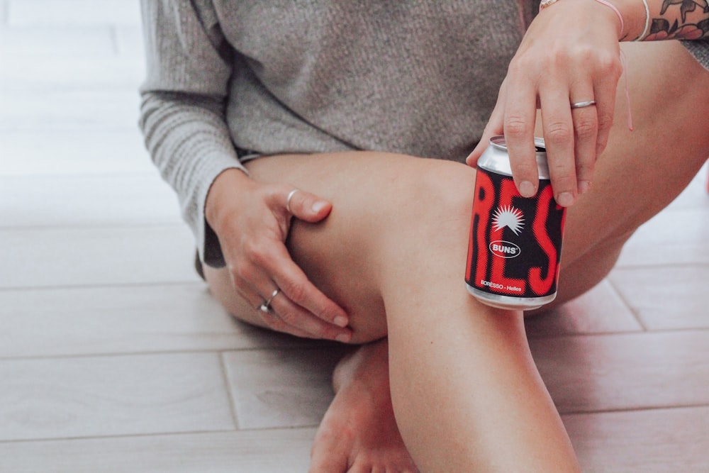 uma mulher sentada no chão segurando uma lata de refrigerante