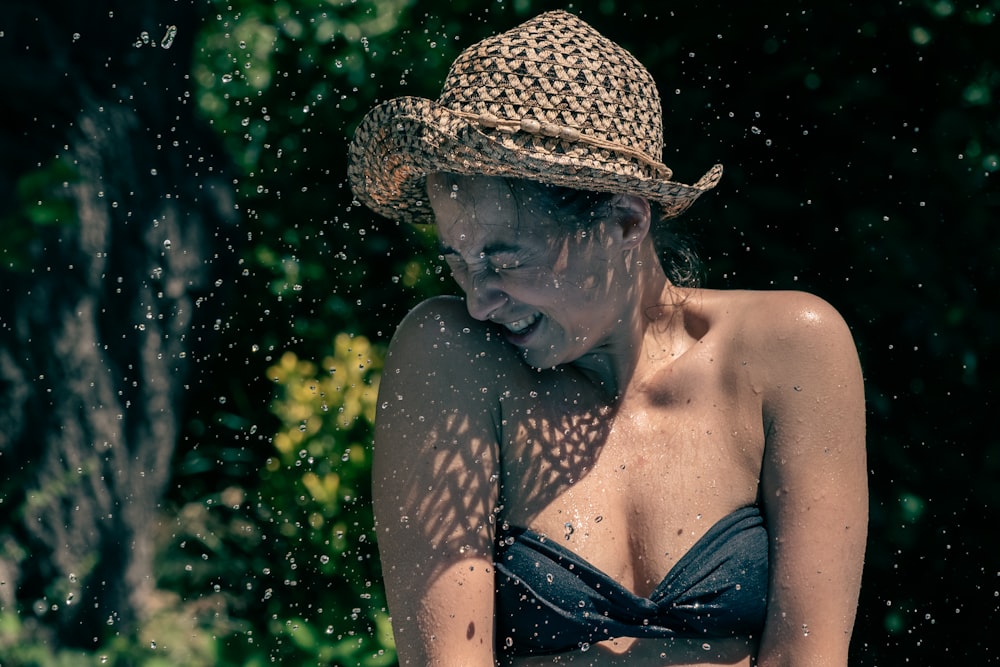a woman in a bikini and straw hat splashing water on her face