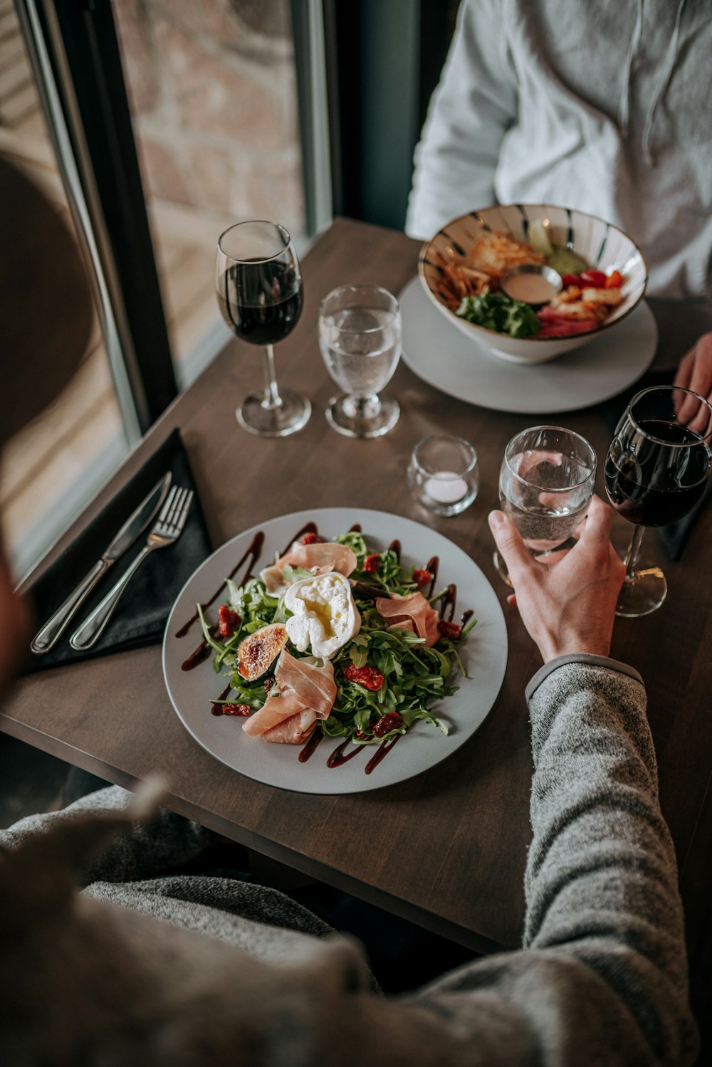 a person sitting at a table with a plate of food and a glass of wine