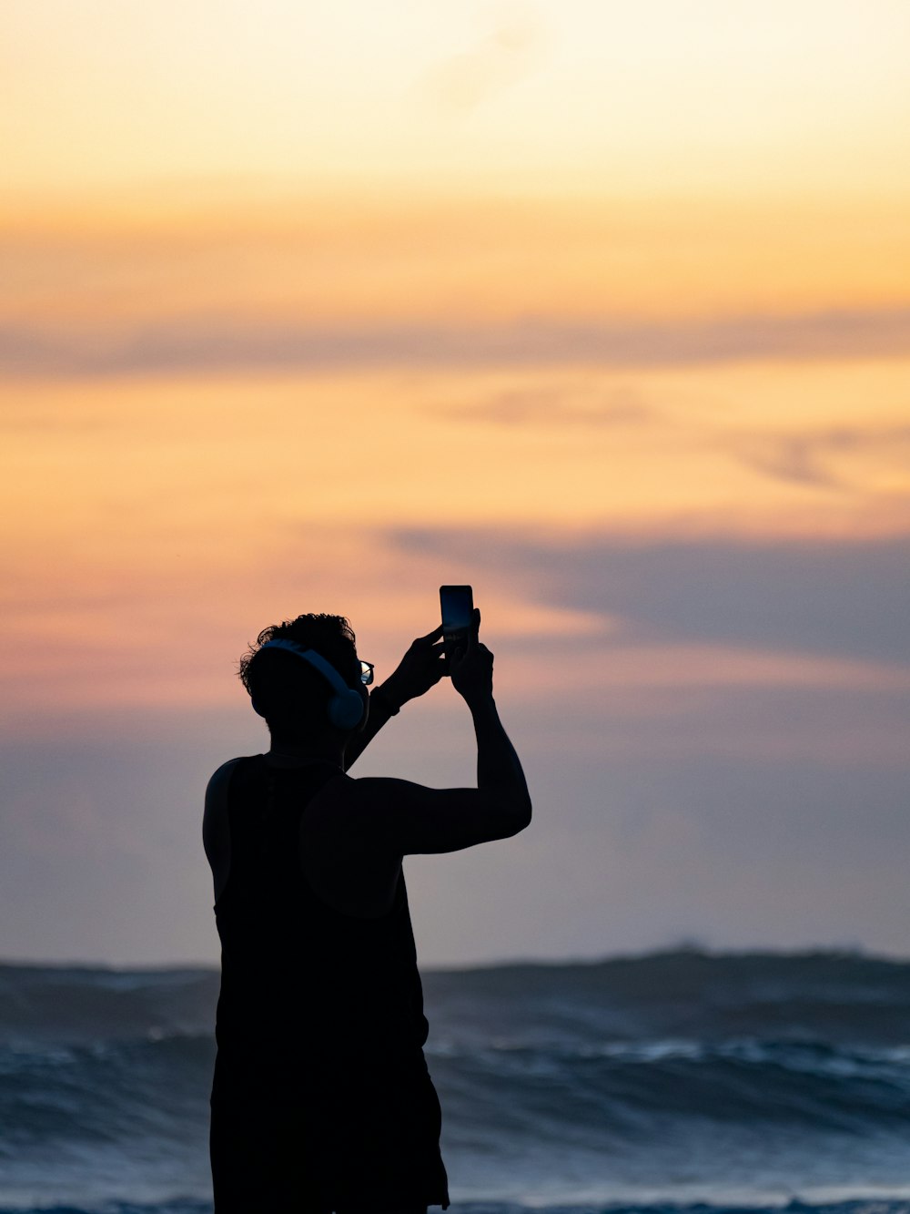 a man standing on a beach taking a picture with a cell phone