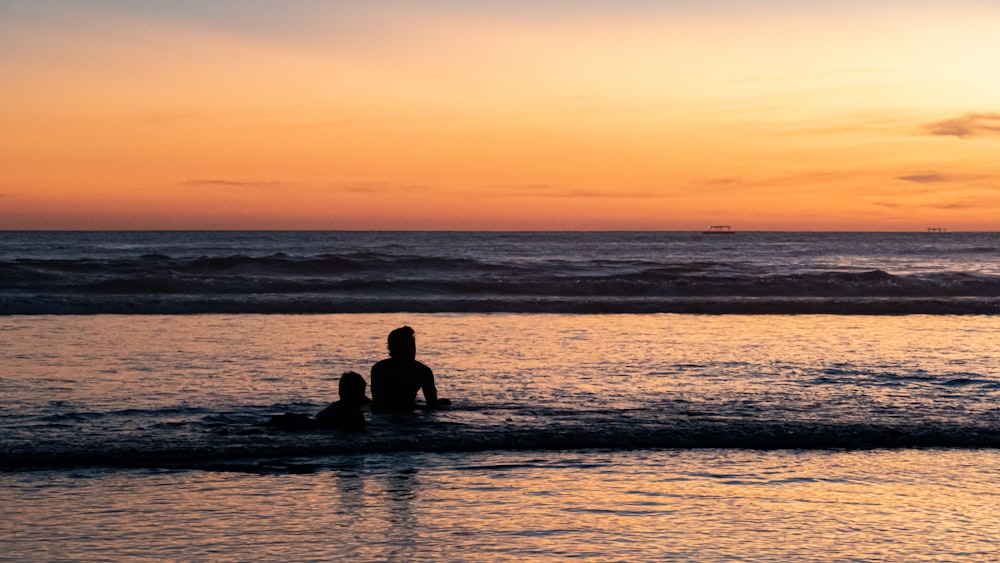 a couple of people sitting on top of a surfboard in the ocean