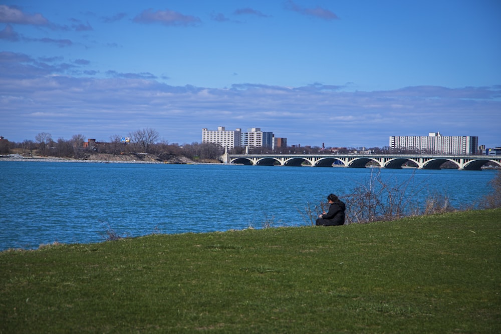 a man sitting on the grass next to a body of water