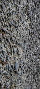 A close-up view of a textured asphalt surface with gravel. The surface is composed of small stones and coarse material, giving a rough appearance.