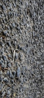 A close-up view of a textured asphalt surface with gravel. The surface is composed of small stones and coarse material, giving a rough appearance.