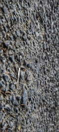 A close-up view of a textured asphalt surface with gravel. The surface is composed of small stones and coarse material, giving a rough appearance.