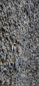 A close-up view of a textured asphalt surface with gravel. The surface is composed of small stones and coarse material, giving a rough appearance.