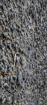 A close-up view of a textured asphalt surface with gravel. The surface is composed of small stones and coarse material, giving a rough appearance.