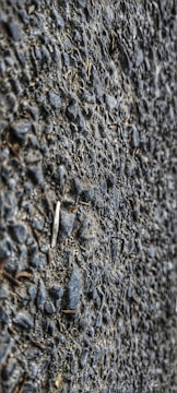 A close-up view of a textured asphalt surface with gravel. The surface is composed of small stones and coarse material, giving a rough appearance.