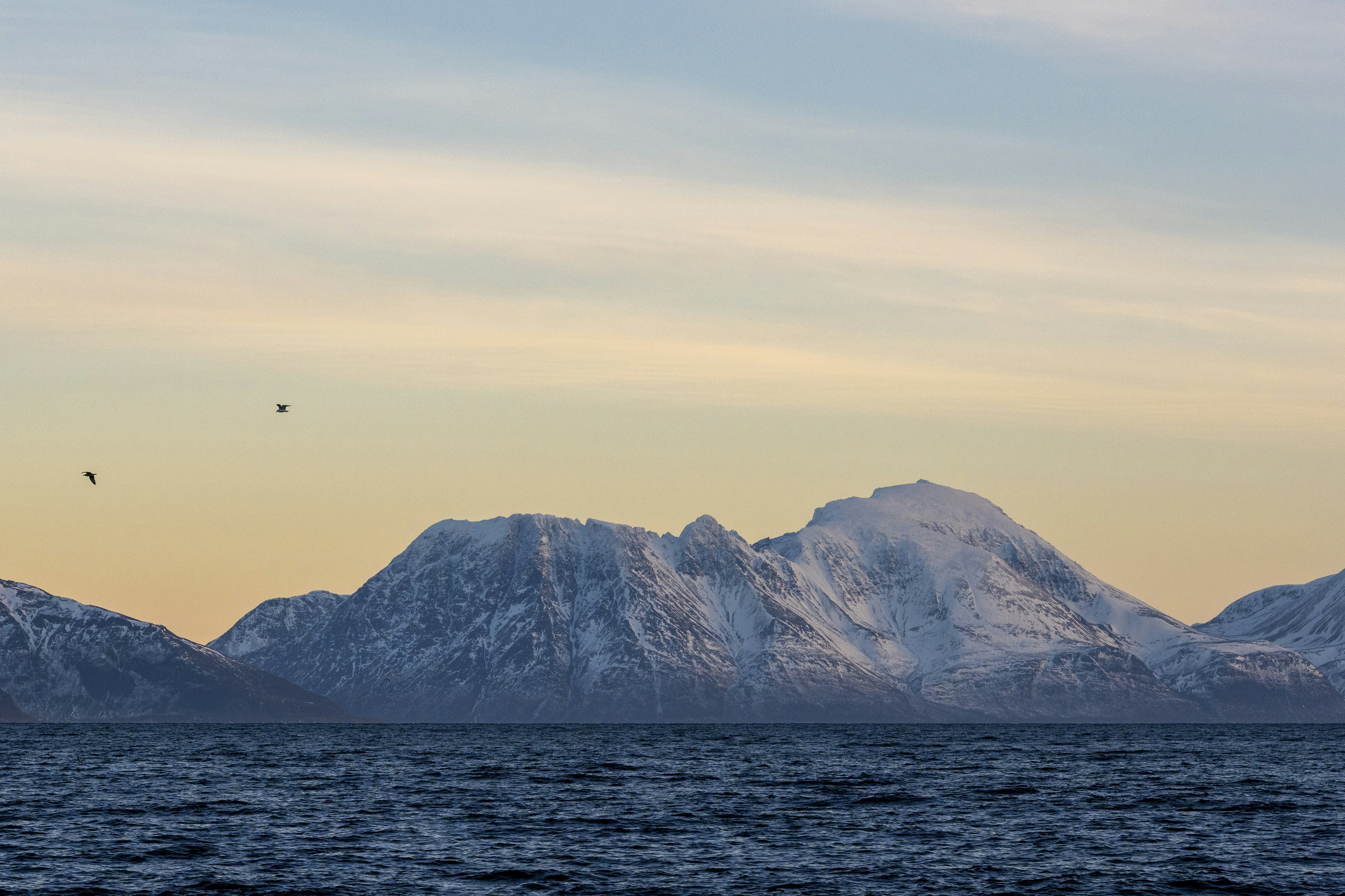 Snow covered mountains by the sea with yellow orange sunset sky 