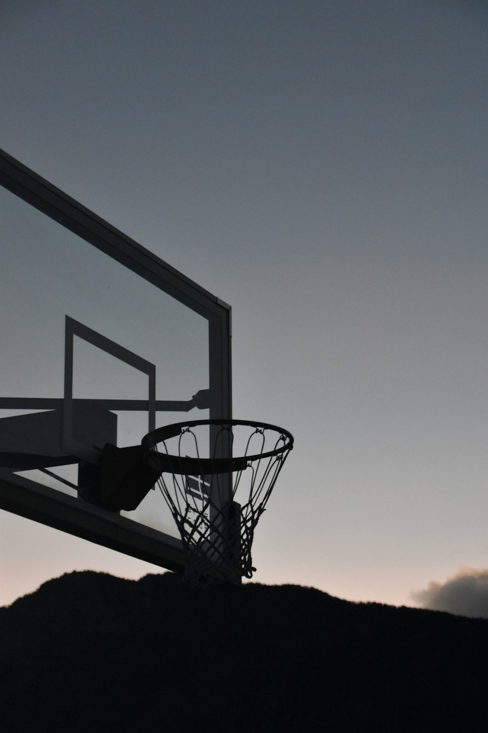 a silhouette of a basketball hoop with a mountain in the background