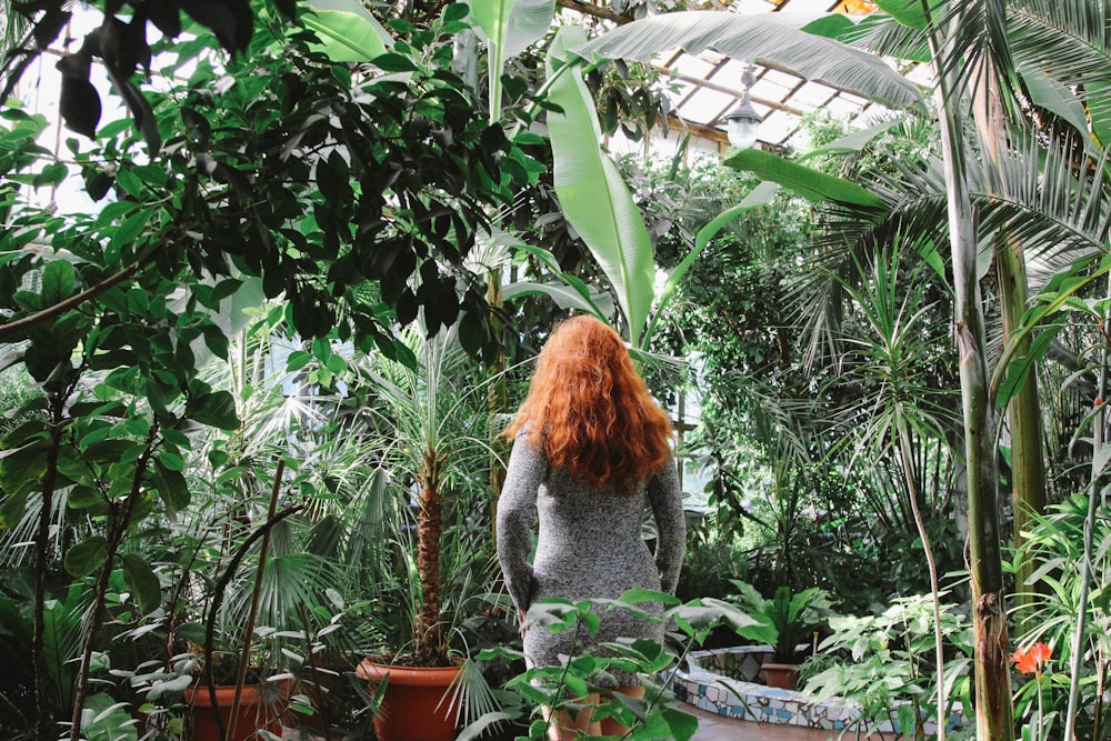 a woman with red hair standing in a greenhouse