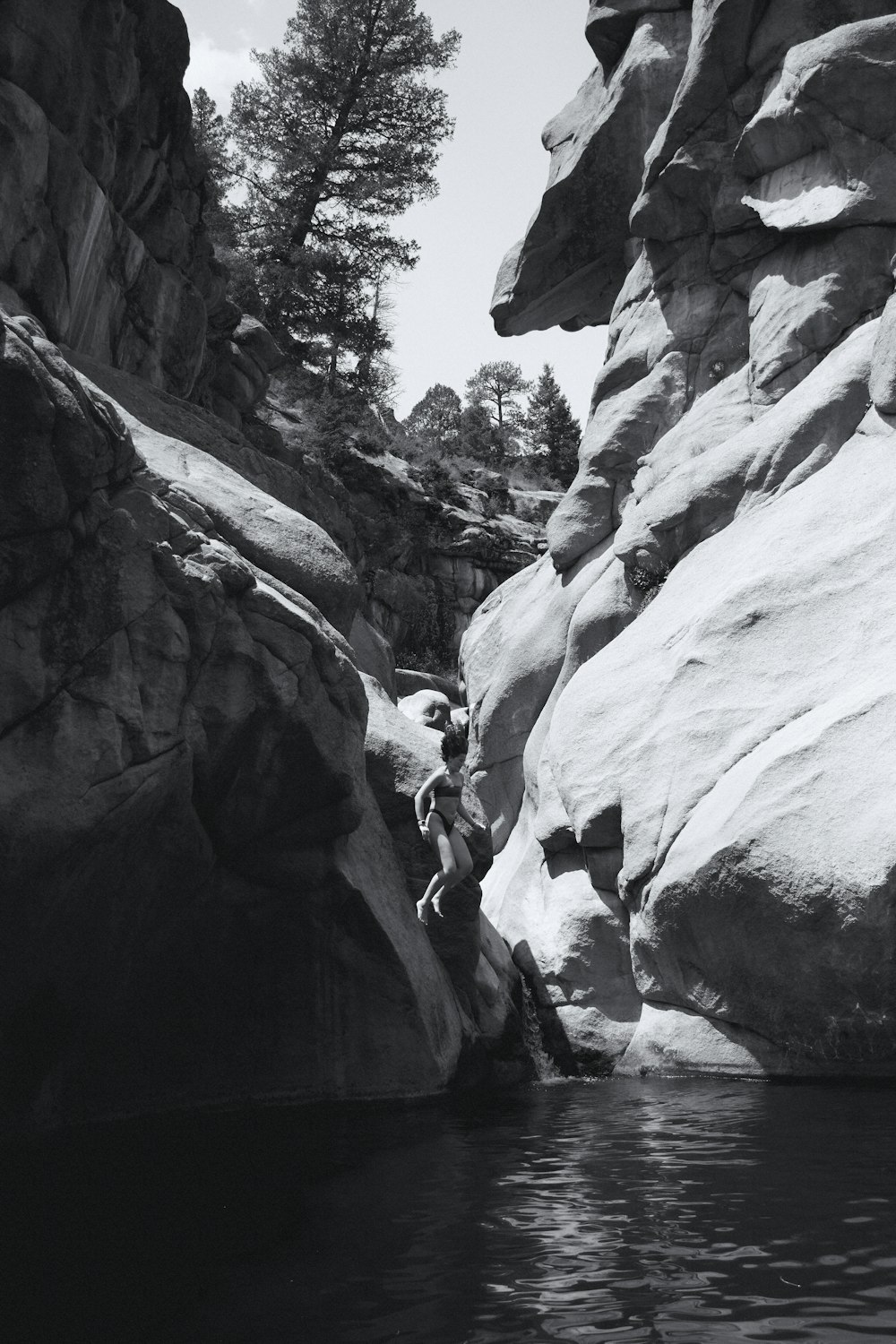 a black and white photo of a person climbing a rock