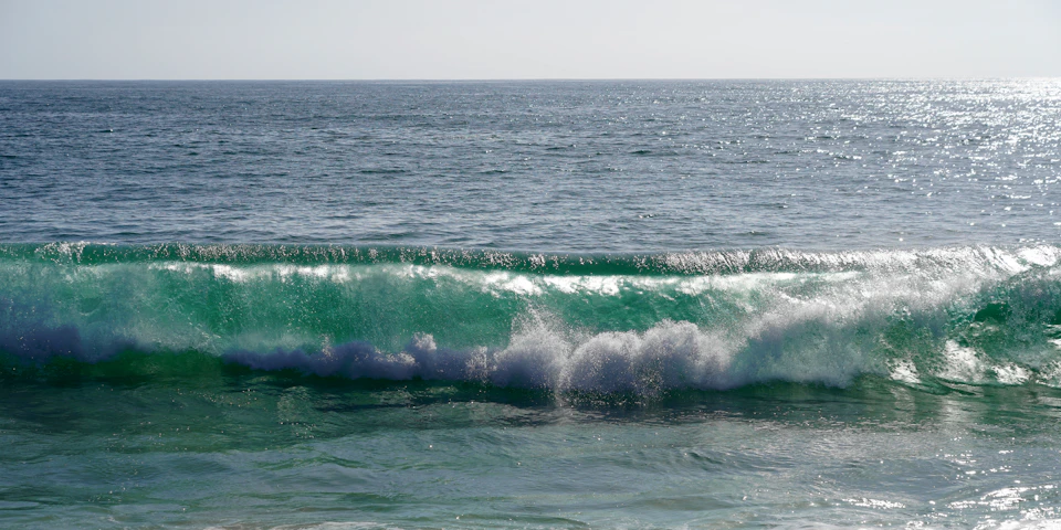 Serene ocean scene with large deep green wave crashing onto the shore